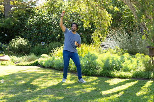 African American man standing on lawn holding orange bubble container and waving bubble wand