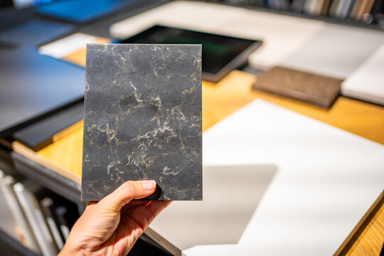 Hand holds dark stone countertop sample while choosing material for kitchen renovation. Surface texture is highlighted with selective focus, shallow depth of field and copy space