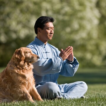 A man in a light blue tai chi practices the 'Pillow Hands' form while his golden retriever sits calmly beside him