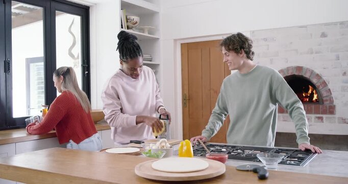 Diverse friends entering from doorway starting pizza prep, African American woman using box grater