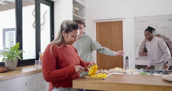 Friends arriving, prepping at island, woman chopping peppers, men passing phone coordinating meal