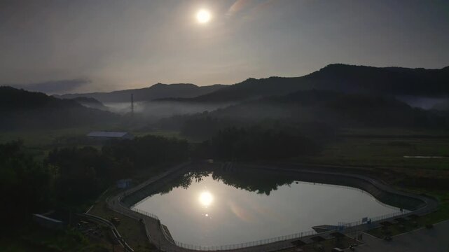 Aerial view of Sriharjo reservoir surrounded by misty hills and lush greenery at sunrise in Imogiri, Special Region of Yogyakarta, Indonesia.