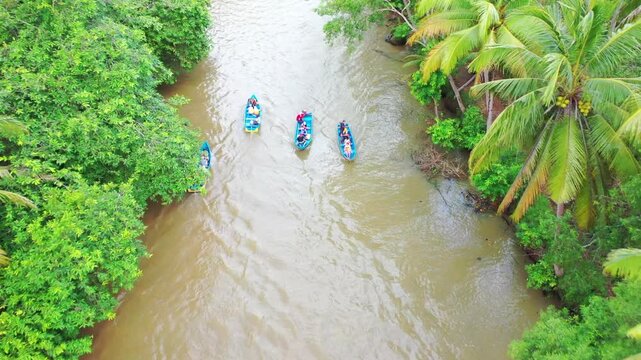 Aerial view of Maron River Pacitan with boats carrying tourists along the lush tropical riverbanks in Kecamatan Pringkuku, Jawa Timur, Indonesia.