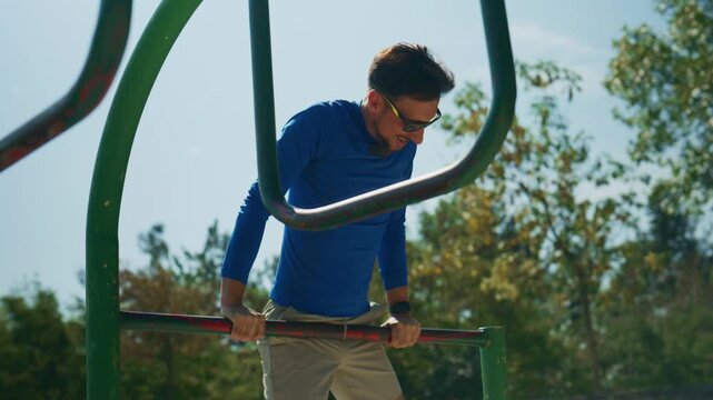 A man in athletic wear performs dips on parallel bars outdoors. He maintains focus during his strength training workout.