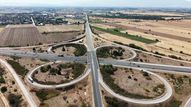 Aerial view of Trakiya Highway cloverleaf interchange surrounded by rural fields and dry landscape in Bulgaria.
