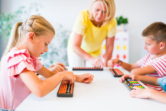 Group of children practicing mental arithmetic and counting with abacuses during a lesson with their teacher in a classroom.