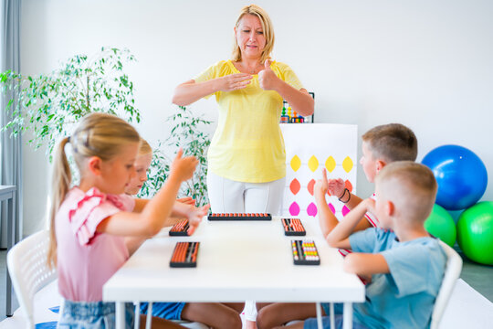 Group of children practicing mental arithmetic and counting with abacuses during a lesson with their teacher in a classroom.
