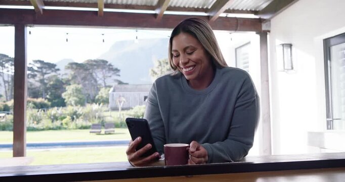 African American woman reading phone, smiling and laughing at message sipping maroon mug on patio