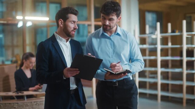 Two Caucasian men businessmen colleagues working together with business papers in office. Boss company CEO leader helping mentoring consulting showing documents terms to intern manager writing notes