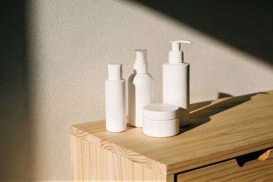 Four white skincare containers in staggered formation on a light wooden surface against a textured beige wall