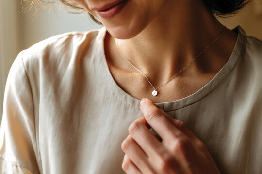 A close-up of a woman wearing a delicate gold necklace while lightly touching her collarbone, conveying a sense of elegance that arises from minimalistic jewelry design.