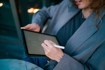 Close up view of Caucasian female freelancer using stylus pen to create digital line art on tablet screen, showcasing remote graphic design workflow and creative digital artwork in city © BullRun