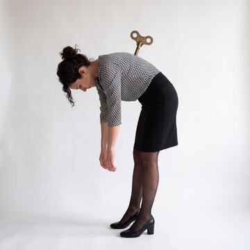 Tired businesswoman bent forward with wind-up key in back symbolizing exhaustion and burnout