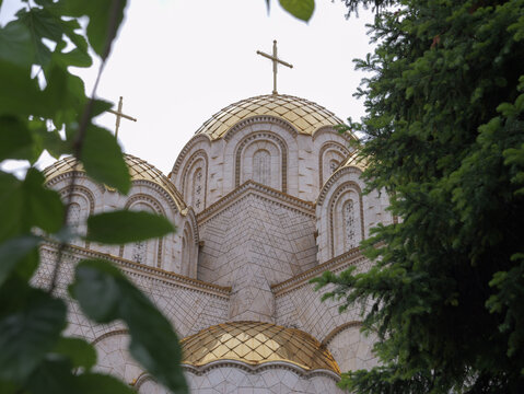 View of Church of Saints Constantine and Helena with golden domes and intricate stone facade framed by green foliage in Shkupi, Qyteti i Shkupit, North Macedonia.