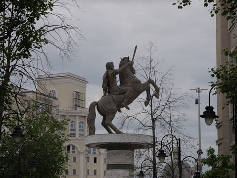 View of the Alexander the Great Statue on its pedestal, surrounded by neoclassical buildings and trees under a cloudy sky in Skopje, Greater Skopje, North Macedonia.
