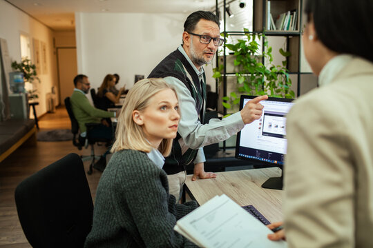 Coworkers discuss project as man points at computer