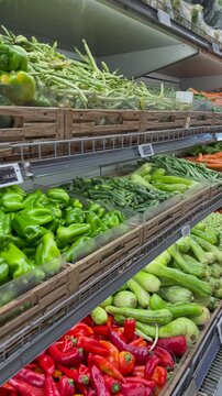 Fresh vegetables fill grocery shelves during camera movement inside supermarket aisle. Colorful bell pepper selections, zucchini and green beans present abundant healthy food retail options.