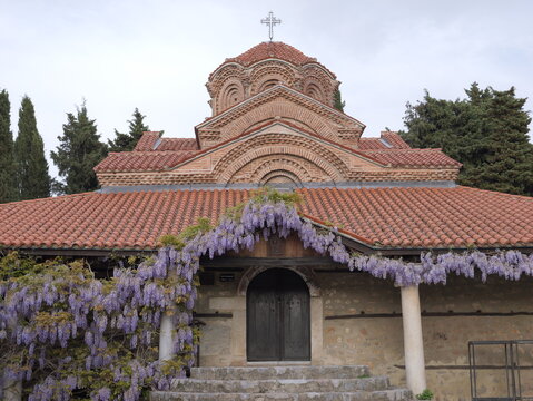 View of the Church of the Virgin Mary Peribleptos featuring a brick dome, terracotta roof, and purple wisteria flowers over the entrance in Ohrid, Municipality of Ohrid, North Macedonia.