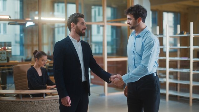 Two Caucasian business men shaking hands meeting in office. Businessmen males workers handshake friendly talking corporate partners smiling shake arms greeting discussing deal agreement partnership