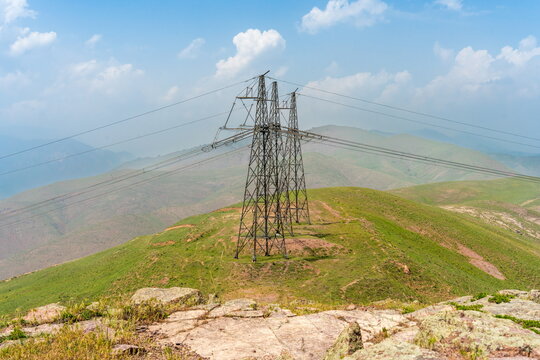 Power transmission towers under white clouds, mountains near Angren