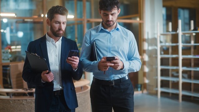 Two gadget addicted Caucasian business men using mobile phones scrolling social media in office. Concentrated businessmen male colleagues workers overuse internet devices app ignoring work in company