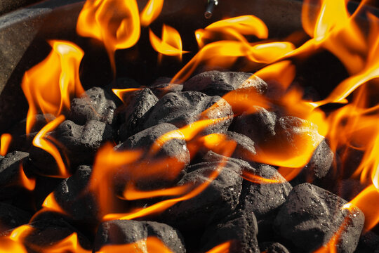 Flaming charcoal briquettes on an outdoor barbecue grill provide heat for cooking.