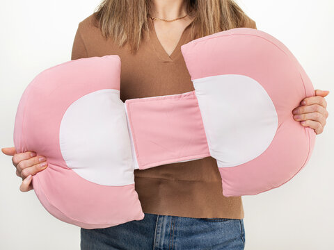 Woman demonstrating pink pregnancy pillow holding it in hands, product photography on light background