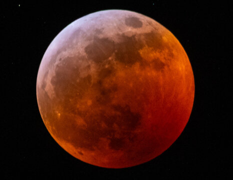 View of the moon during a total lunar eclipse with a reddish hue against the dark night sky in Canada.