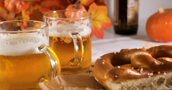 Person serving pretzels on a wooden board with beer mugs on an autumn tablecloth, illustrating national Bavarian culinary heritage