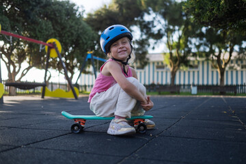 Cute Little Girl in Blue Helmet Sitting on Penny Board at Playground Outdoors © RealPeopleStudio