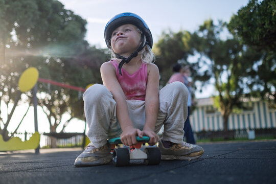 Cute Little Girl in Blue Helmet Sitting on Penny Board at Playground Outdoors