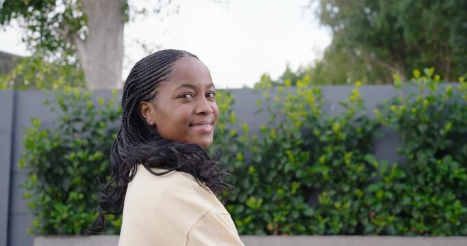 Woman turning head toward camera, responding to camera movement, smiling and laughing by gray fence