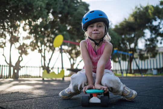 Cute Little Girl in Blue Helmet Sitting on Penny Board at Playground Outdoors