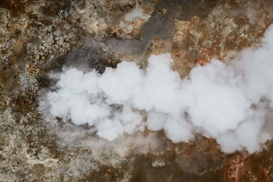 Aerial view of geothermal steam rising from volcanic ground with rocky terrain and mineral deposits in Reykjavik, Reykjavikurborg, Iceland.