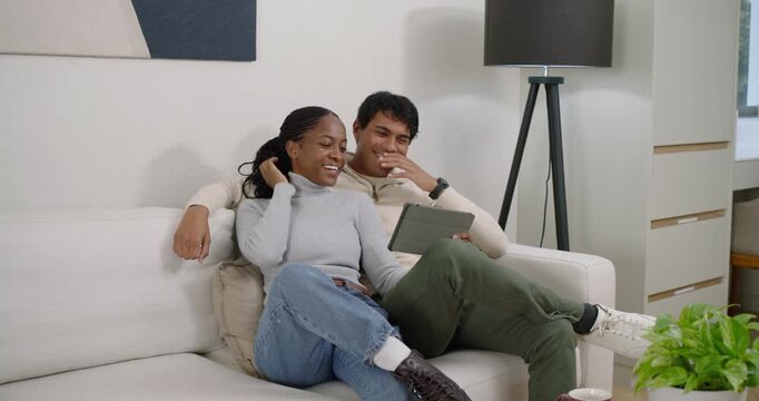 Couple sitting on white sofa viewing and sharing tablet clip, woman tapping, man cuddling