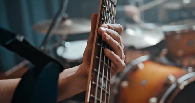 Close-up of Musician Playing Bass Guitar in Music Studio with Blurred Drum Kit Background