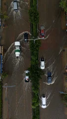 An elevated view of a flooded road with vehicles driving through the water. © eakarat