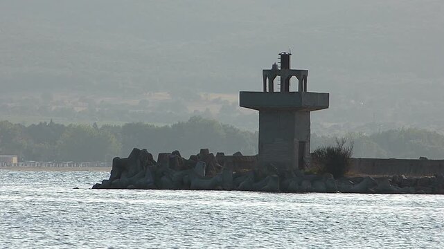 Medium shot of a coastal lighthouse with calm sea surf and tiny waves on a cloudy afternoon
