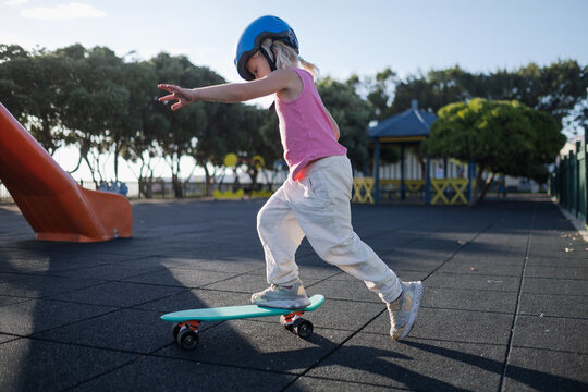 Little Girl in Blue Helmet Riding Penny Board and Balancing at Playground