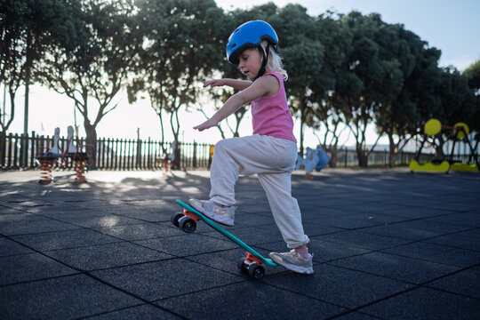 Little Girl in Blue Helmet Riding Penny Board and Balancing at Playground