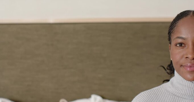 Adult African woman on bed in sweater, reacting to offscreen cue, smiling then laughing, copy space