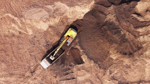 Aerial view of an excavator loading soil into a dump truck at a construction site in India.