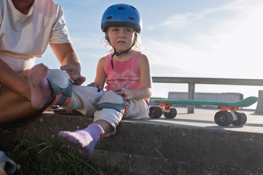 Caring parent Putting Knee Pads and Safety Protection on Little Daughter Before Skateboarding 