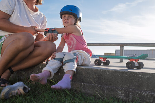 Caring parent Putting Knee Pads and Safety Protection on Little Daughter Before Skateboarding 
