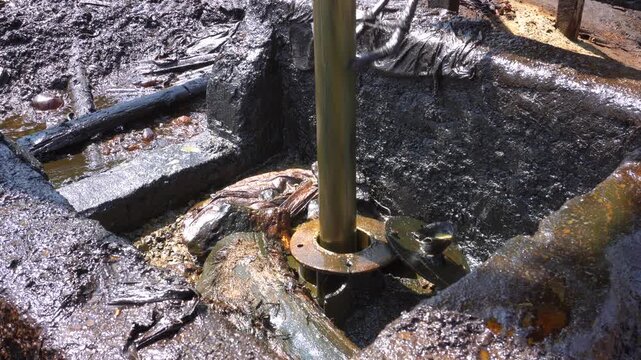 Traditional crude oil extraction from deep well at Teksas Wonocolo mining field in Bojonegoro, East Java, Indonesia. Raw black petroleum pulling process using traditional pipe rig in a rural area.