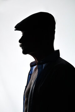 Dramatisches Silhouettenportr&auml;t eines &auml;lteren Mannes mit Schieberm&uuml;tze und Sakko im Seitenprofil. Low-Key, Schatten, Charakter, Vintage-Stil, geheimnisvolle Stimmung und Studiofotografie.