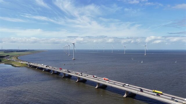 Aerial view of Ketelbrug bridge with traffic crossing over the water, surrounded by offshore wind turbines under a blue sky in Nagele, Flevoland, Netherlands.