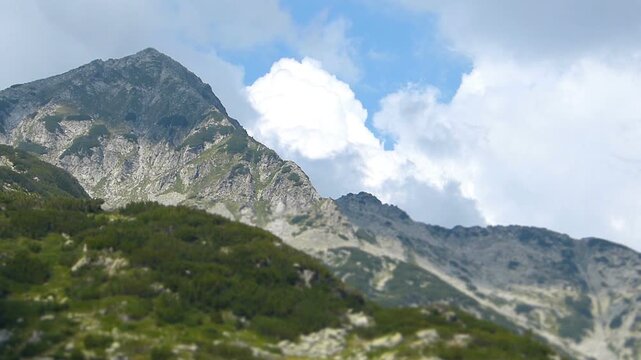 Miniature tilt shift effect of a Pirin mountain peak in Bulgaria under a blue sky with moving clouds in August

