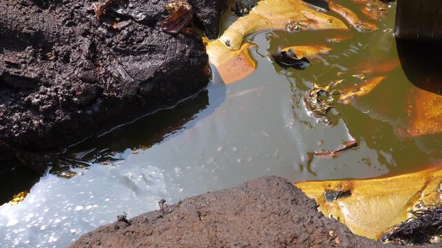 Crude oil flows through a ditch channel to a storage container at Teksas Wonocolo traditional oil mining field in Bojonegoro, East Java, Indonesia, showcasing traditional petroleum extraction methods.