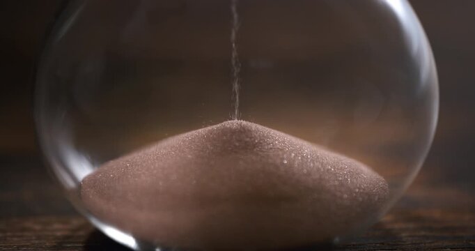 Cinematic slow motion close-up of an hourglass with sand falling through the narrow passage, symbolizing the passage of time, mortality, patience and the fleeting nature of life. 1000 fps.